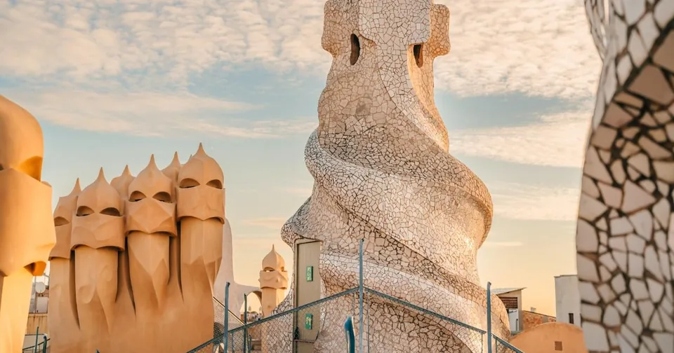 Verdrehte cremefarbene Dachschornsteine und ein mosaikverkleideter Turm vor einem blassen Himmel
