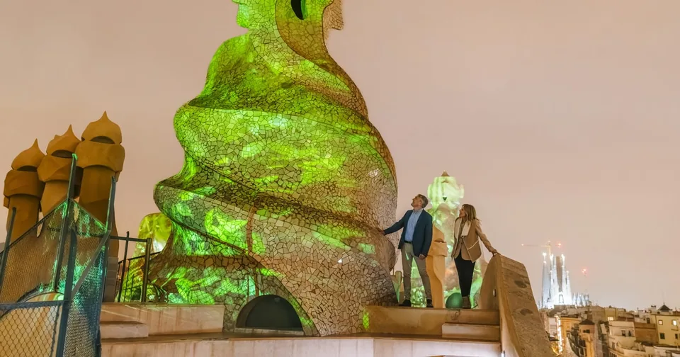 Besucher auf einem Dach neben einem verdrehten Schornstein, der bei Dämmerung in grünem Licht beleuchtet ist
